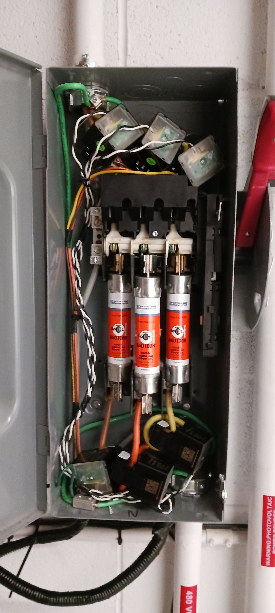 Open combiner box interior showing fuses, terminal blocks, and grounding conductors
