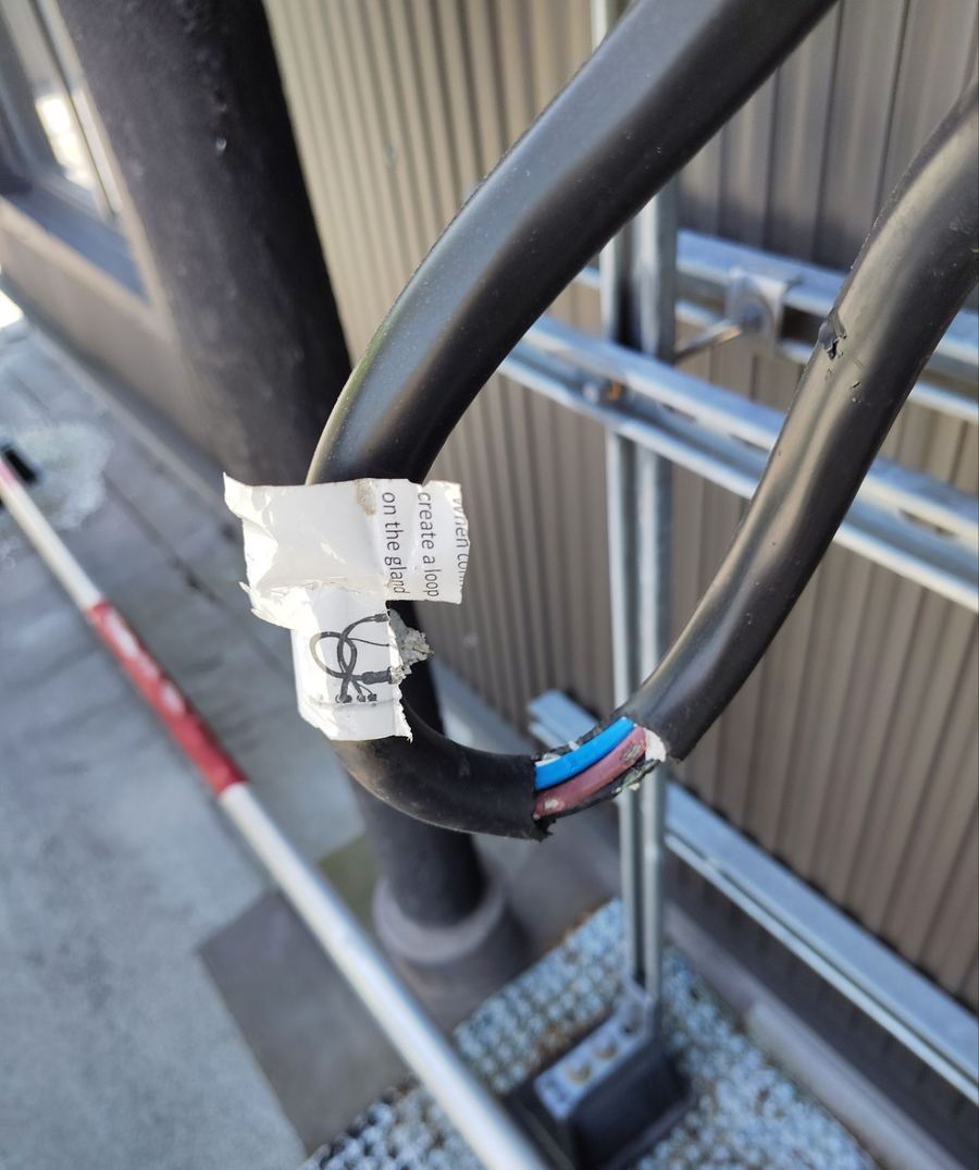 Damaged conduit gland with exposed, unterminated conductors at a rooftop mounting rail
