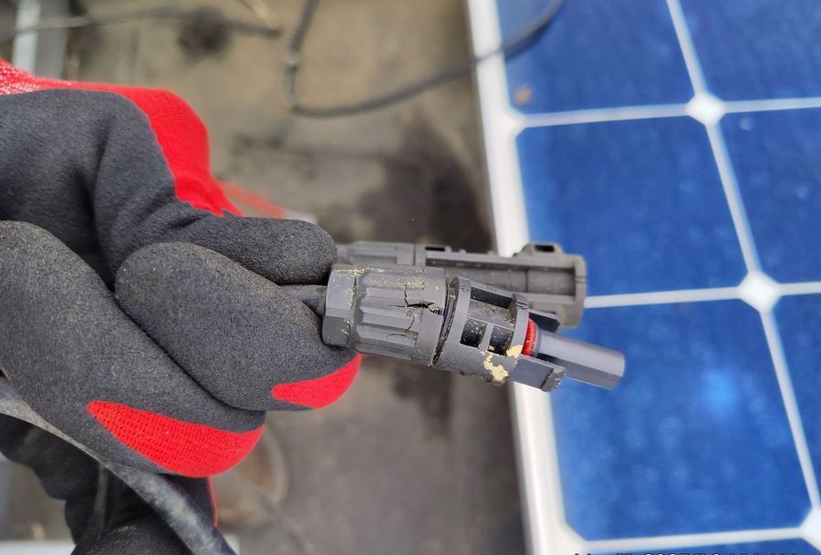 Cracked MC4 connector housing on a solar panel, held in a gloved hand