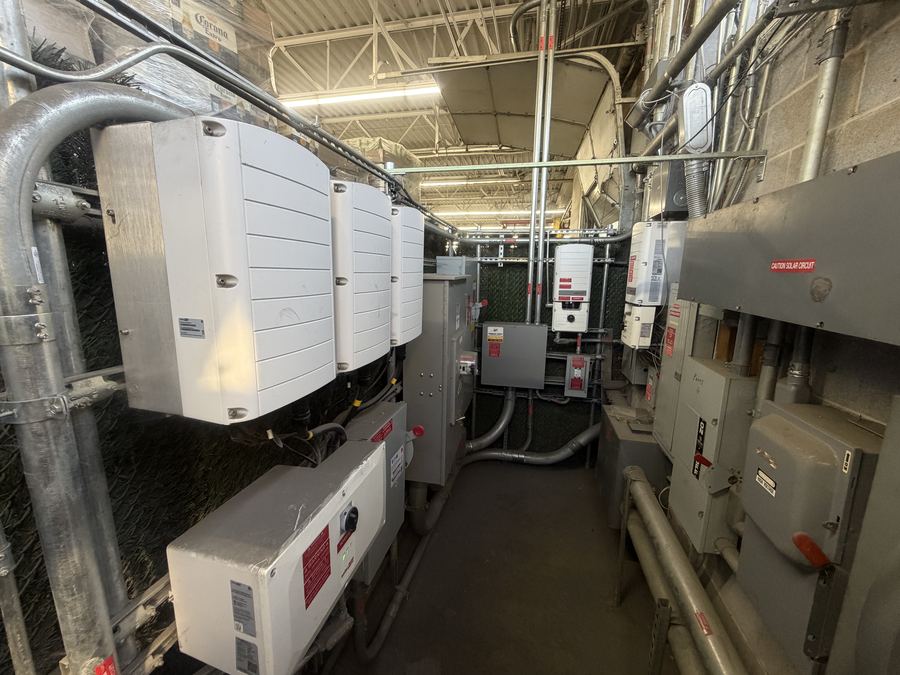 Row of three commercial SolarEdge inverters mounted in a mechanical room with conduit and disconnects