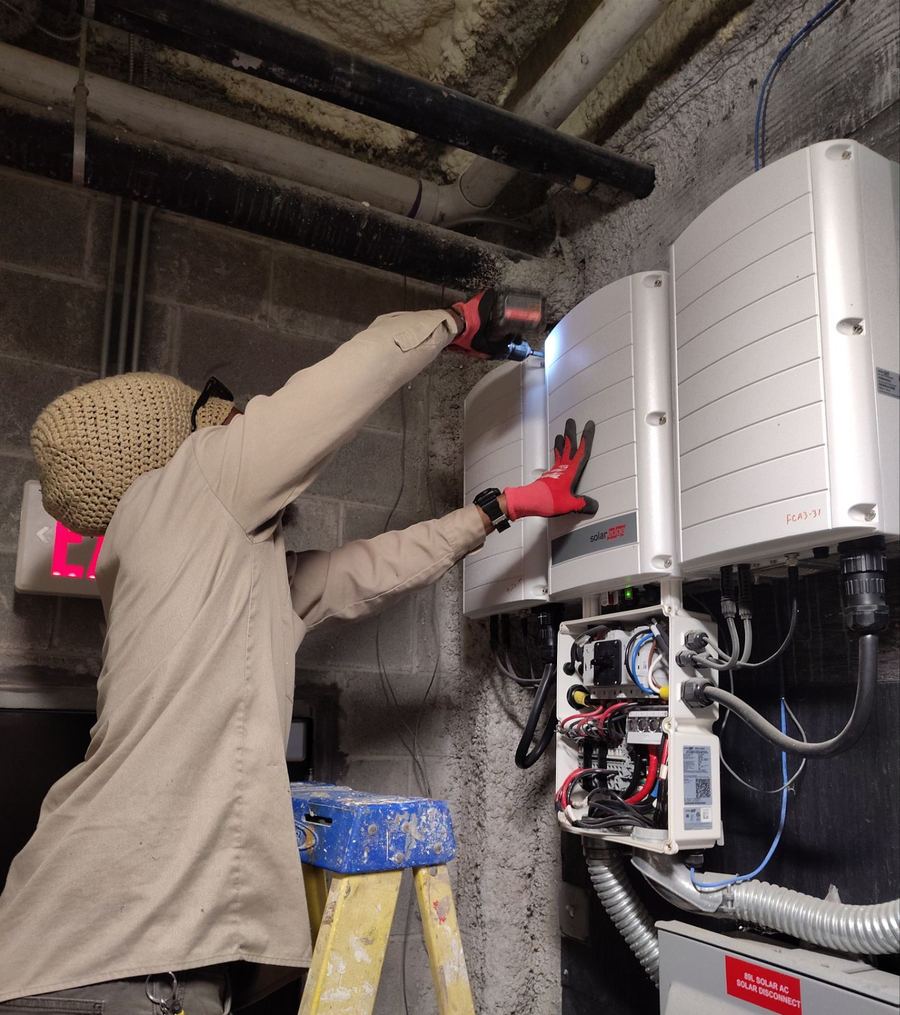 Technician working on a wall-mounted SolarEdge inverter installation in a mechanical room